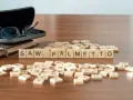 Fichas de madera deletrean "SAW PALMETTO" junto a un libro y gafas.