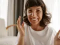 Mujer sonriente aplicándose crema en la mejilla, como si fueran vitaminas para el sol.