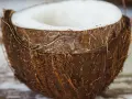 Mitad de coco con pulpa blanca visible. La cáscara fibrosa y marrón resalta las propiedades del coco, un tesoro tropical.