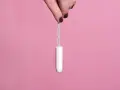 Mano sujetando un tampón blanco con hilo azul sobre fondo rosa. Existen diversos tipos de tampones para cada necesidad.