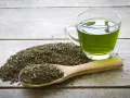 Té verde en una taza de cristal y una cuchara de madera con hojas secas. Descubre qué es el EGCG y sus beneficios.