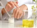 Manos de científico aplicando crema, con tubos de ensayo y líquidos amarillos. El cetearyl alcohol es clave en esta formulación.