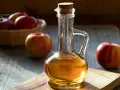Botella de vinagre de manzana con manzanas rojas frescas. Descubre los 10 beneficios del vinagre de manzana.