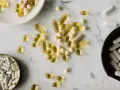 Pastillas y cápsulas de suplementos, algunas amarillas y otras blancas, dispersas sobre una superficie de mármol. ¿NMN qué es?