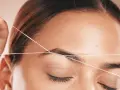 Detalle de depilación hilo en cejas. Una mano sostiene un hilo para perfilar la forma de la ceja, logrando un acabado preciso y natural.