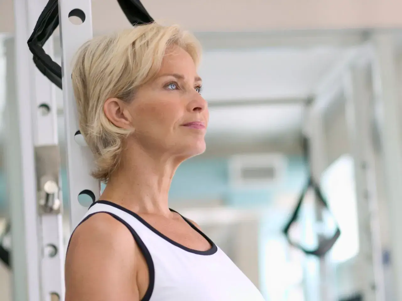 Mujer rubia en gimnasio, pensando en cómo tomar fat burner para mejorar su rutina de ejercicios.