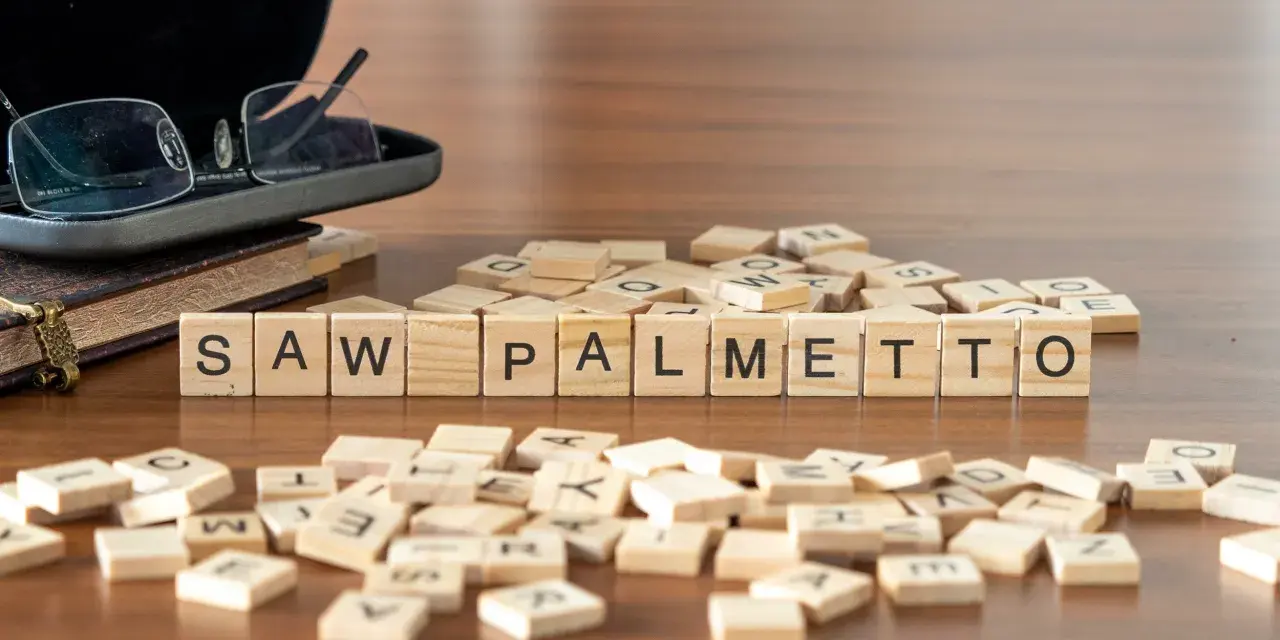 Fichas de madera deletrean "SAW PALMETTO" junto a un libro y gafas.