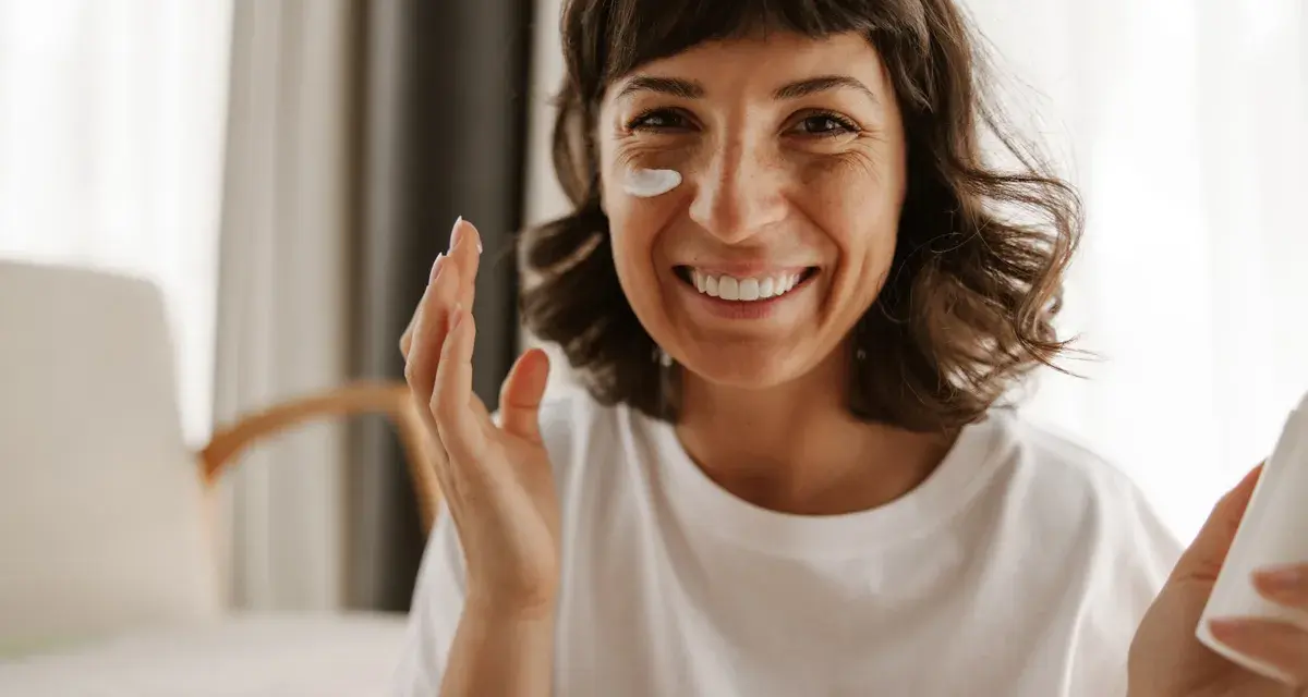 Mujer sonriente aplicándose crema en la mejilla, como si fueran vitaminas para el sol.