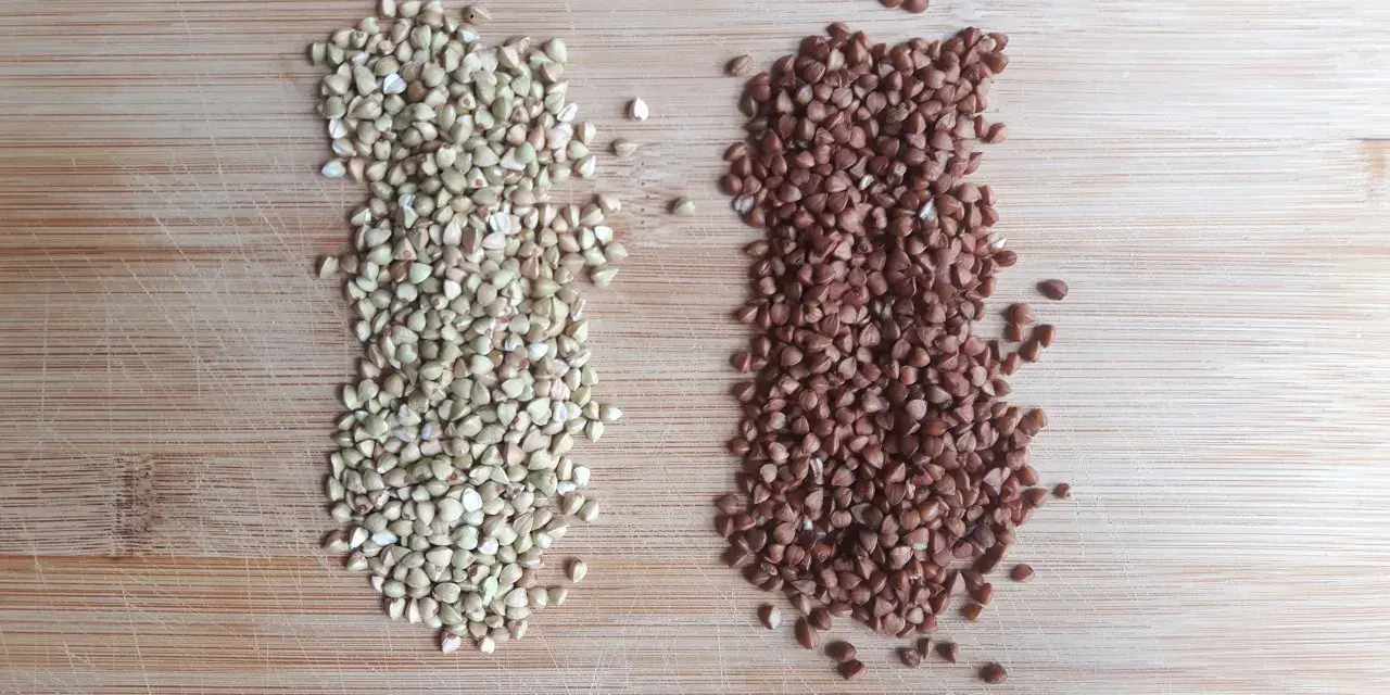 Dos montones de alforfón, uno verde y otro tostado, sobre una tabla de madera. ¿Alforfón que es? Un grano nutritivo.