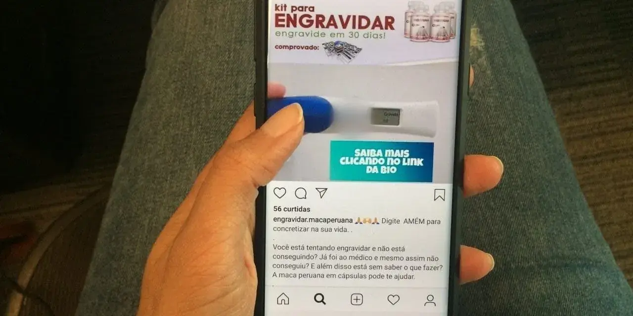 Mano sosteniendo un teléfono que muestra un anuncio de "kit para engravidar" y un test de embarazo. La maca peruana en cápsulas puede ayudar a quienes buscan el embarazo.