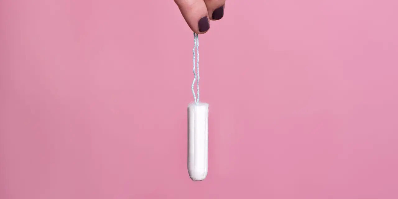 Mano sujetando un tampón blanco con hilo azul sobre fondo rosa. Existen diversos tipos de tampones para cada necesidad.