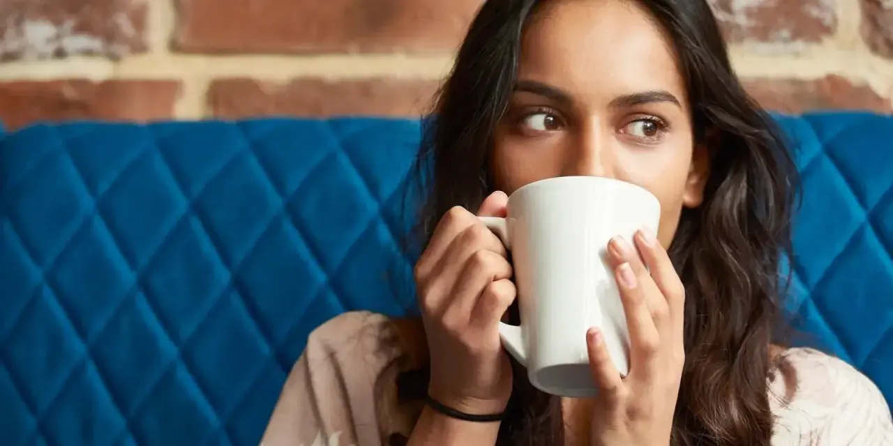 Mujer con taza blanca, quizás probando una bebida sin cafeína para superar la abstinencia de cafeína.