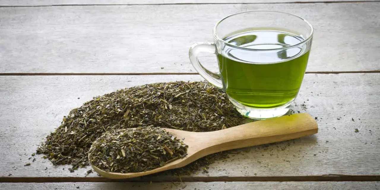 Té verde en una taza de cristal y una cuchara de madera con hojas secas. Descubre qué es el EGCG y sus beneficios.