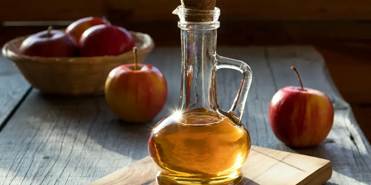 Botella de vinagre de manzana con manzanas rojas frescas. Descubre los 10 beneficios del vinagre de manzana.