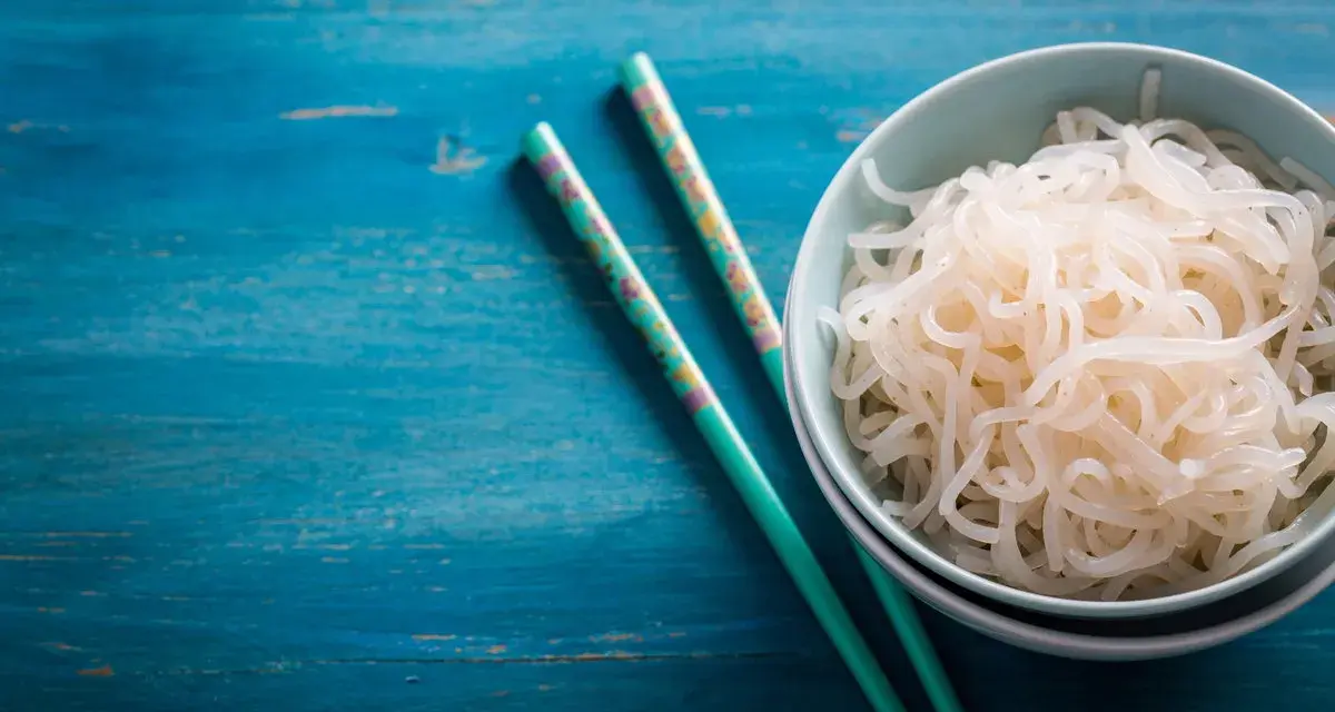 Un tazón de fideos konjac, ideal para una dieta saludable durante el embarazo, junto a palillos decorados sobre una mesa azul.