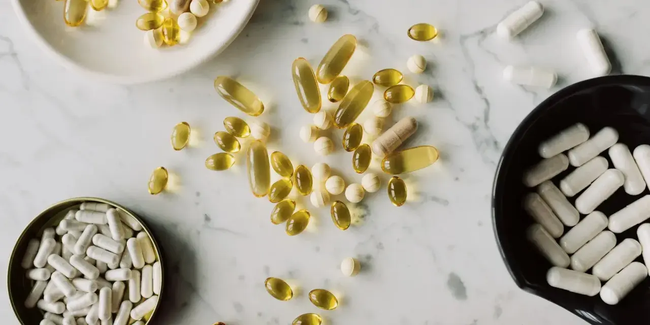 Pastillas y cápsulas de suplementos, algunas amarillas y otras blancas, dispersas sobre una superficie de mármol. ¿NMN qué es?