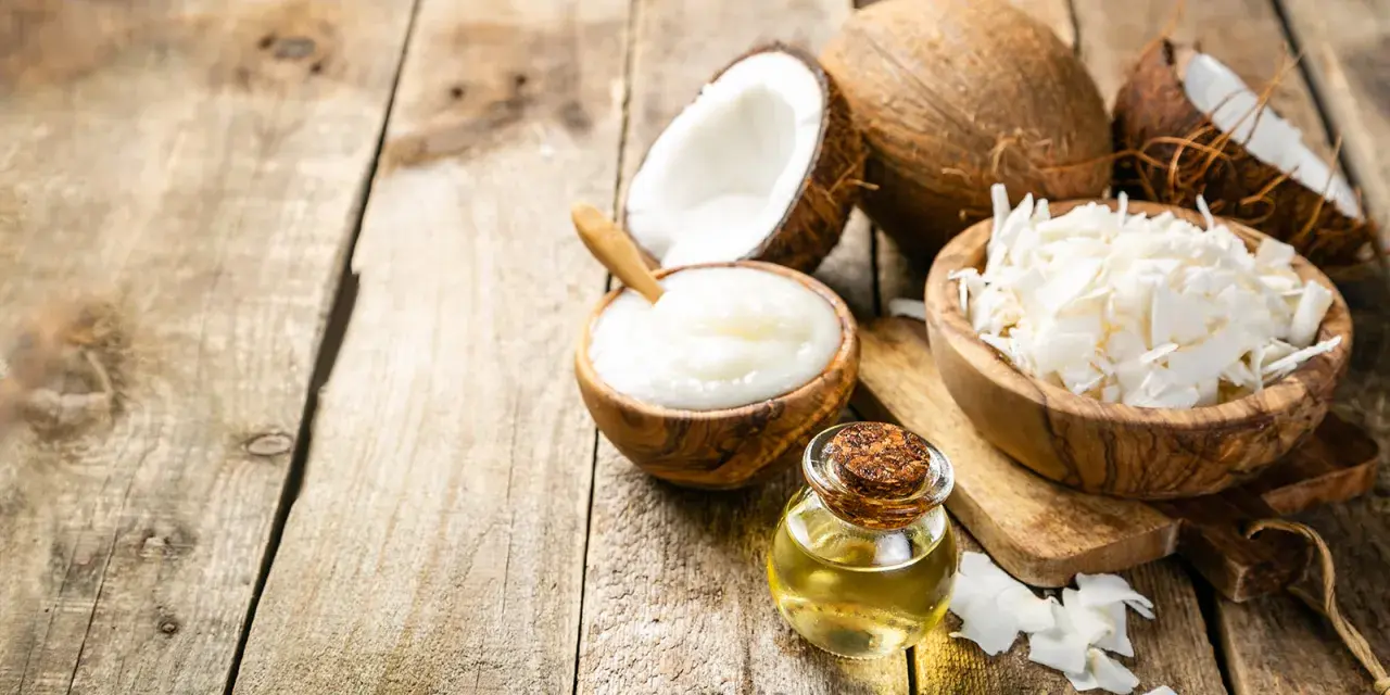 Aceite MCT en una botella junto a cocos partidos, crema de coco y coco rallado sobre madera rústica.