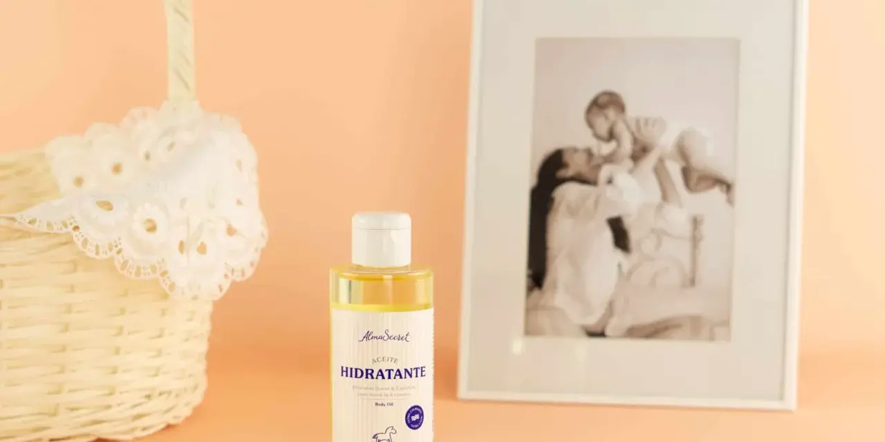 Aceite hidratante de almendras, ideal para el cuidado de la piel durante el embarazo. Junto a una cesta y un marco con foto familiar.