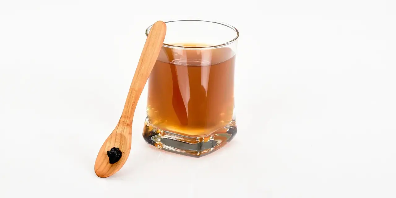 Vaso con bebida dorada y cuchara de madera con shilajit. Descubre los shilajit beneficios para la mujer.