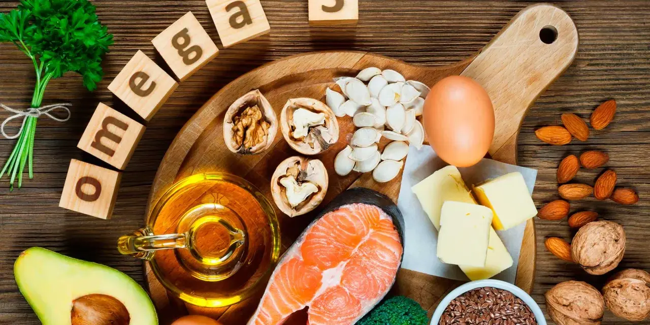 Bloques de madera deletrean "omega 3" junto a salmón, aguacate, nueces, semillas, huevos y aceite, mostrando alimentos ricos en omega 3.