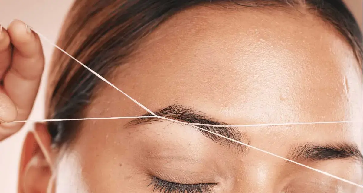 Detalle de depilación hilo en cejas. Una mano sostiene un hilo para perfilar la forma de la ceja, logrando un acabado preciso y natural.