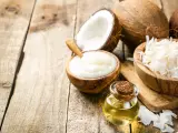 Aceite MCT en una botella junto a cocos partidos, crema de coco y coco rallado sobre madera rústica.