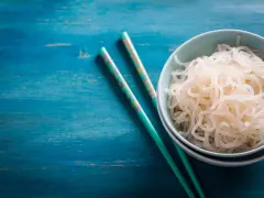 Un tazón de fideos konjac, ideal para una dieta saludable durante el embarazo, junto a palillos decorados sobre una mesa azul.