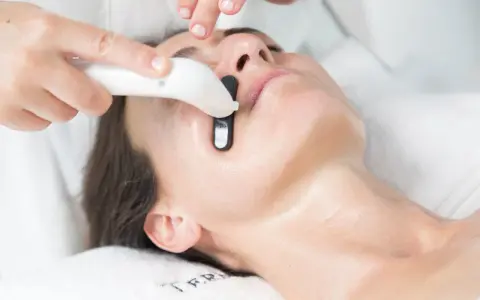 Una persona recibe un tratamiento facial en casa con un dispositivo que emite luz.