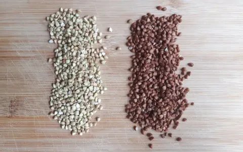 Dos montones de alforfón, uno verde y otro tostado, sobre una tabla de madera. ¿Alforfón que es? Un grano nutritivo.