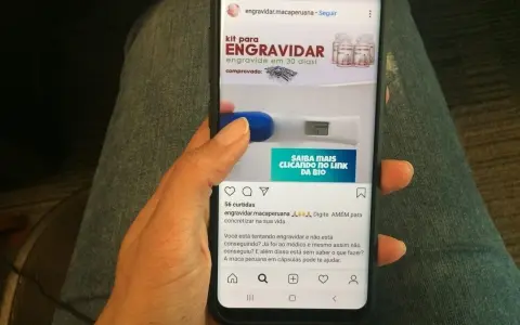 Mano sosteniendo un teléfono que muestra un anuncio de "kit para engravidar" y un test de embarazo. La maca peruana en cápsulas puede ayudar a quienes buscan el embarazo.