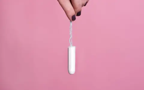 Mano sujetando un tampón blanco con hilo azul sobre fondo rosa. Existen diversos tipos de tampones para cada necesidad.