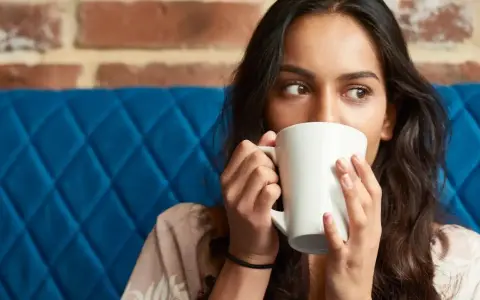 Mujer con taza blanca, quizás probando una bebida sin cafeína para superar la abstinencia de cafeína.