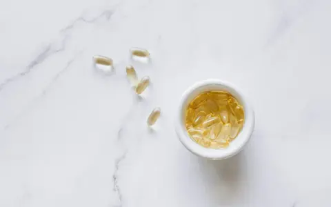 Cápsulas amarillas en un cuenco blanco y dispersas sobre mármol. Podrían ser suplementos de quercetina, investigando sus efectos secundarios.