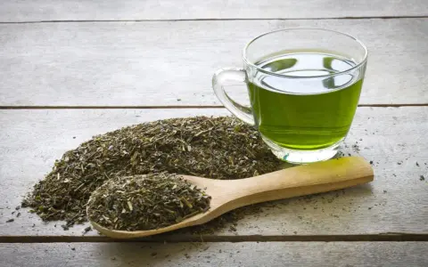 Té verde en una taza de cristal y una cuchara de madera con hojas secas. Descubre qué es el EGCG y sus beneficios.