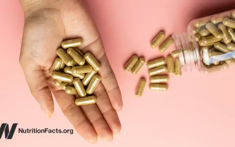 Una mano sostiene cápsulas doradas. Una botella volcada derrama más cápsulas. ¿Se puede tomar ginseng y maca a la vez?