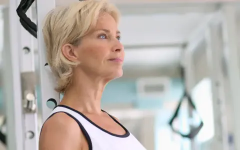 Mujer rubia en gimnasio, pensando en cómo tomar fat burner para mejorar su rutina de ejercicios.
