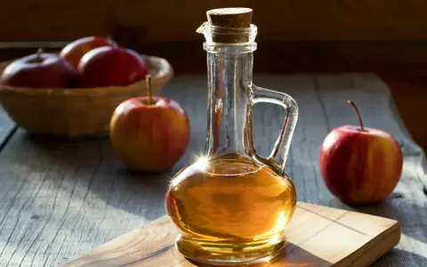 Botella de vinagre de manzana con manzanas rojas frescas. Descubre los 10 beneficios del vinagre de manzana.