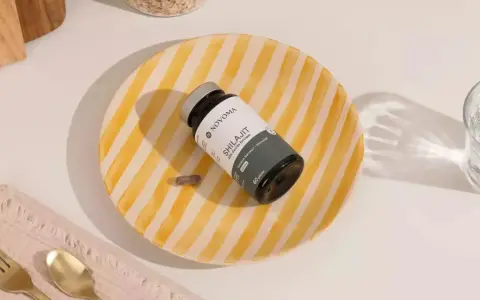 Un frasco de Shilajit y una cápsula sobre un plato rayado. Descubre para qué sirve el shilajit y cómo puede beneficiar tu sistema nervioso e inmunológico.