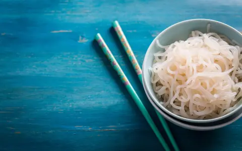 Un tazón de fideos konjac, ideal para una dieta saludable durante el embarazo, junto a palillos decorados sobre una mesa azul.
