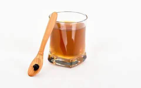 Vaso con bebida dorada y cuchara de madera con shilajit. Descubre los shilajit beneficios para la mujer.