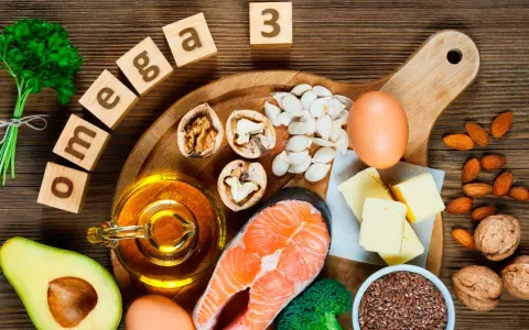 Bloques de madera deletrean "omega 3" junto a salmón, aguacate, nueces, semillas, huevos y aceite, mostrando alimentos ricos en omega 3.
