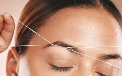 Detalle de depilación hilo en cejas. Una mano sostiene un hilo para perfilar la forma de la ceja, logrando un acabado preciso y natural.
