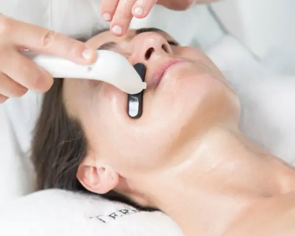 Una persona recibe un tratamiento facial en casa con un dispositivo que emite luz.