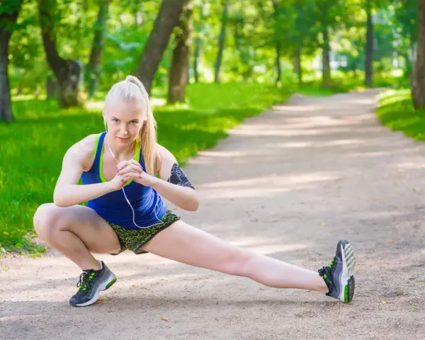 Mujer rubia haciendo estiramientos laterales en un parque, un ejercicio ideal para mejorar el sistema linfático y la flexibilidad.