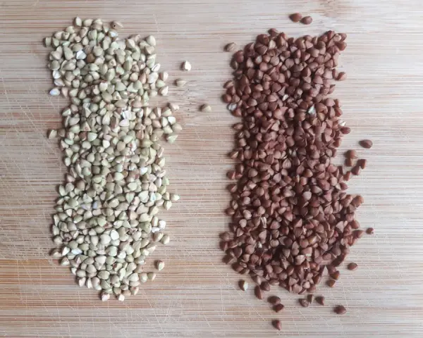 Dos montones de alforfón, uno verde y otro tostado, sobre una tabla de madera. ¿Alforfón que es? Un grano nutritivo.