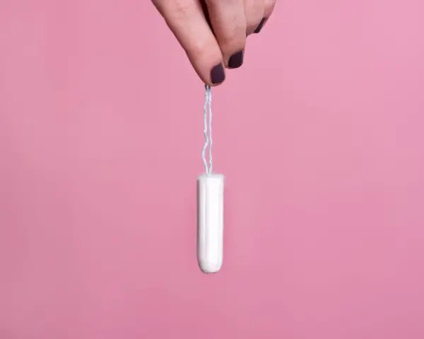 Mano sujetando un tampón blanco con hilo azul sobre fondo rosa. Existen diversos tipos de tampones para cada necesidad.