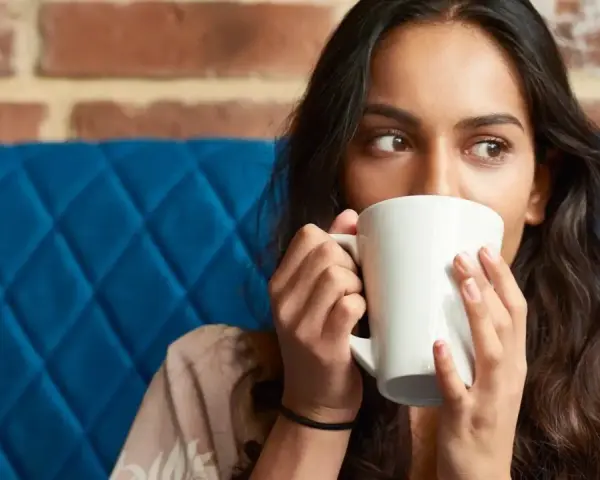 Mujer con taza blanca, quizás probando una bebida sin cafeína para superar la abstinencia de cafeína.