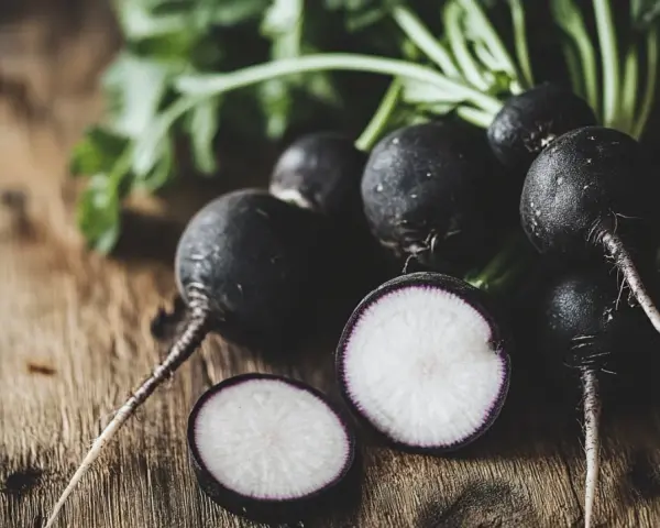Un grupo de rábanos negros con sus hojas verdes sobre una mesa de madera. Uno está cortado, mostrando su interior blanco y morado.