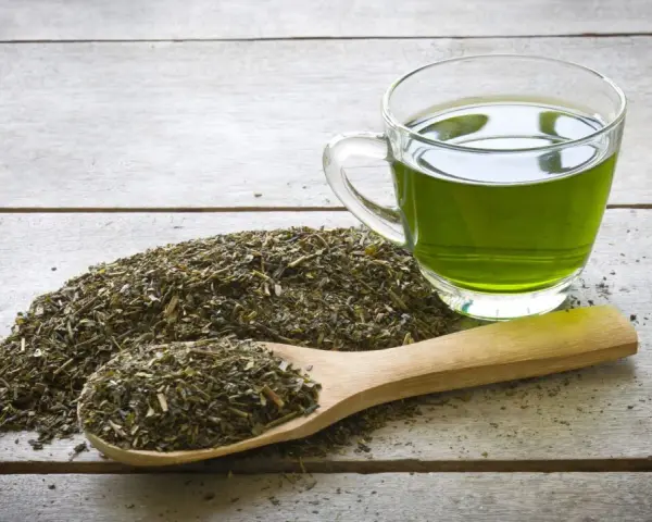 Té verde en una taza de cristal y una cuchara de madera con hojas secas. Descubre qué es el EGCG y sus beneficios.