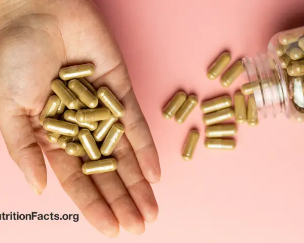 Una mano sostiene cápsulas doradas. Una botella volcada derrama más cápsulas. ¿Se puede tomar ginseng y maca a la vez?